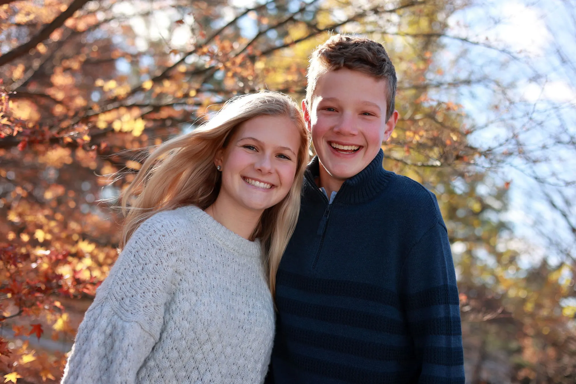 A teenage brother and sister smiling among red autumn leaves