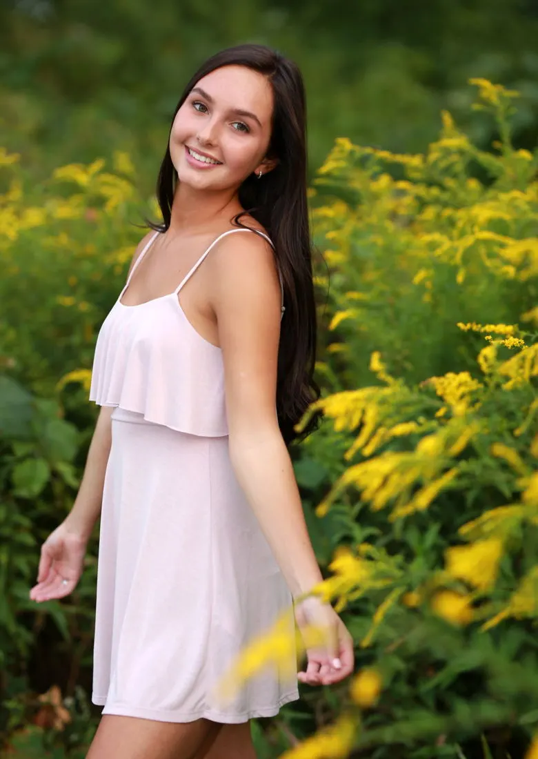 A high-school senior in a white dress among yellow wildflowers